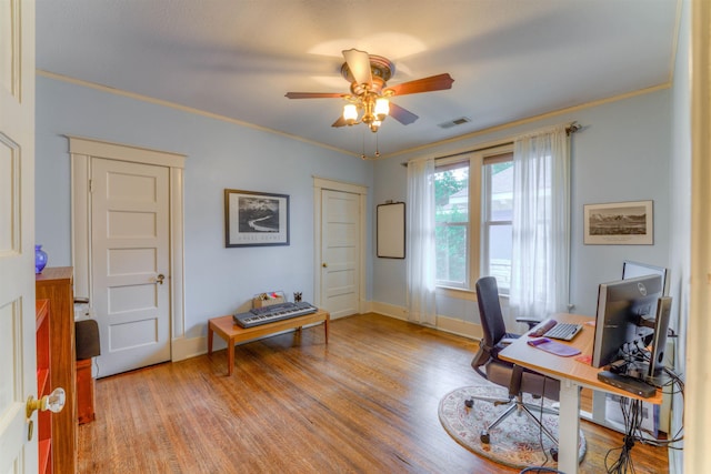 office featuring light wood-style floors, crown molding, ceiling fan, and visible vents