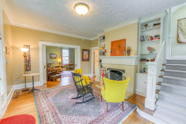 living area with crown molding, a brick fireplace, wood finished floors, and stairway