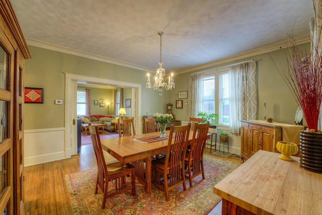 dining space with a chandelier, ornamental molding, light wood-style flooring, and a wainscoted wall