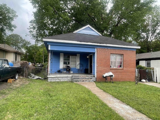 back of house featuring a porch, a lawn, fence, and brick siding