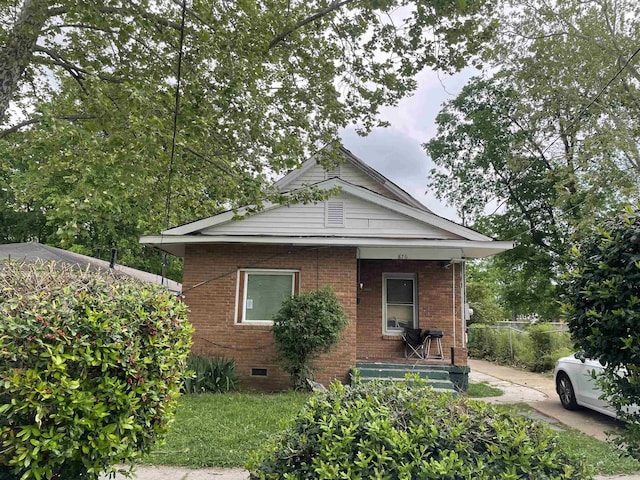 bungalow featuring brick siding, covered porch, and crawl space