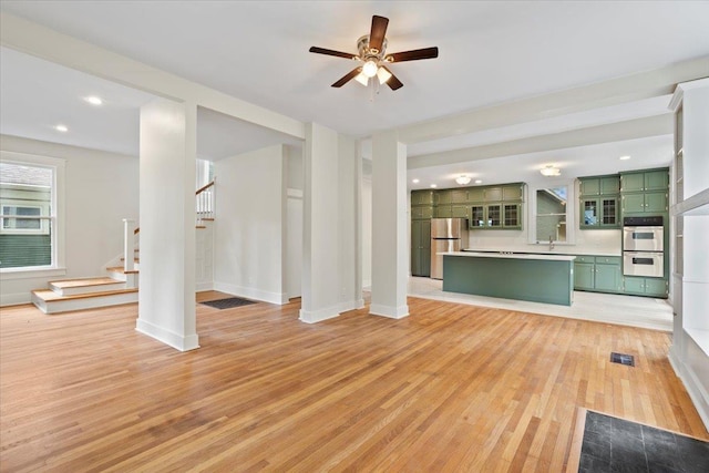 1682 Lawrence Ave, Memphis, TN 38112 - unfurnished living room featuring ceiling fan, a sink, baseboards, light wood-style floors, and stairs