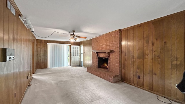 unfurnished living room featuring carpet flooring, wood walls, ceiling fan, and a brick fireplace