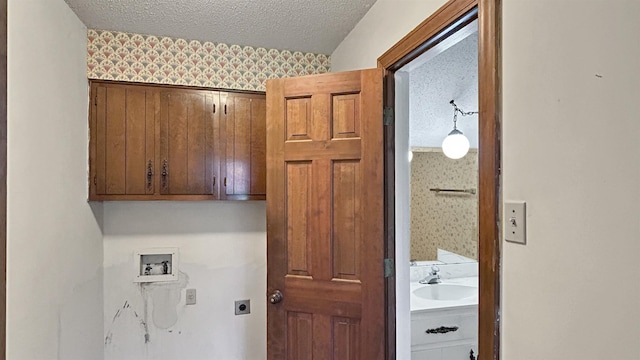 clothes washing area with wallpapered walls, a textured ceiling, washer hookup, cabinet space, and electric dryer hookup