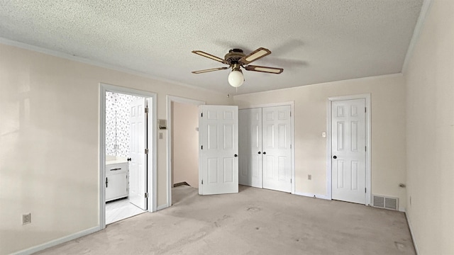 unfurnished bedroom with connected bathroom, visible vents, baseboards, light carpet, and ornamental molding
