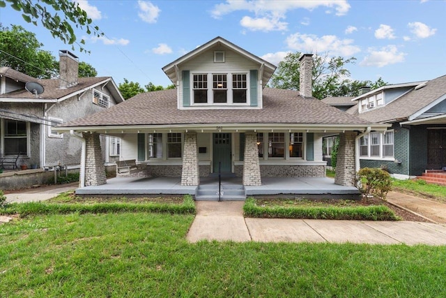 view of front of home with roof with shingles, covered porch, a chimney, and a front lawn