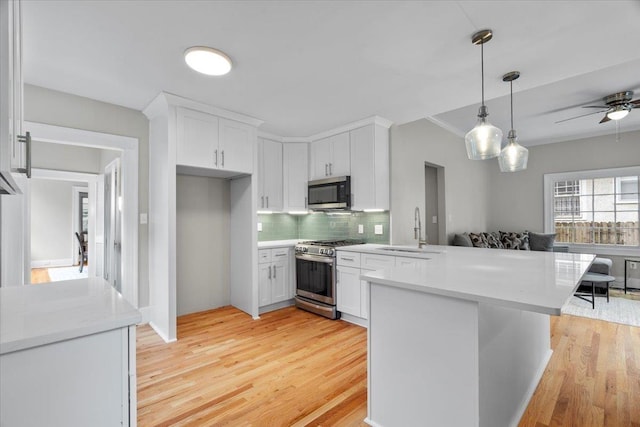 kitchen with white cabinetry, a sink, a peninsula, stainless steel appliances, and light wood-style flooring