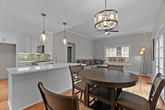 dining area with crown molding, light wood finished floors, ceiling fan with notable chandelier, and baseboards