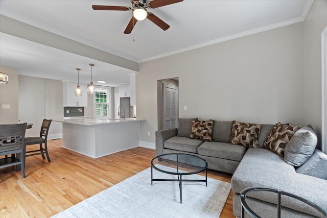 living room featuring light wood-type flooring, ornamental molding, baseboards, and a ceiling fan