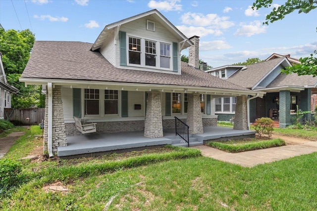 view of front of home featuring a porch, a shingled roof, a front lawn, and stone siding