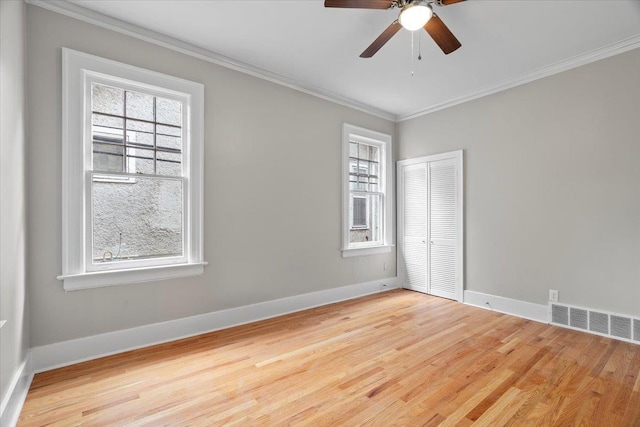 empty room featuring a wealth of natural light, ornamental molding, wood finished floors, and visible vents