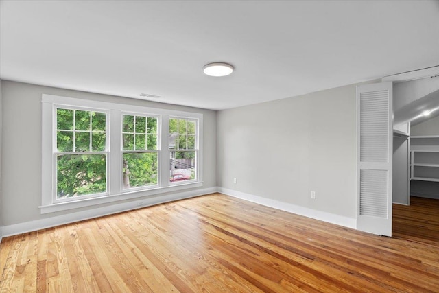 unfurnished room with baseboards, visible vents, a healthy amount of sunlight, and wood finished floors