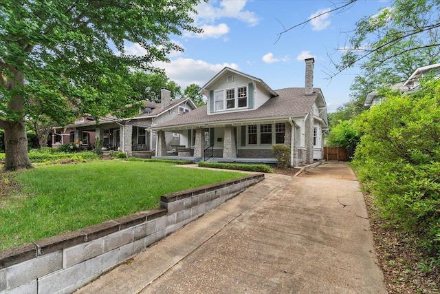 view of front facade with fence, a front lawn, stone siding, a chimney, and covered porch