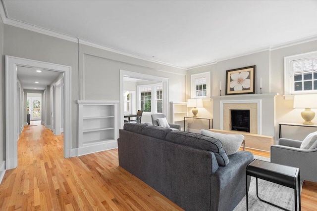 living room with crown molding, a fireplace, light wood finished floors, and built in shelves