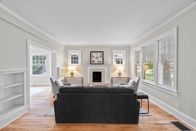 living area with light wood finished floors, a fireplace with raised hearth, baseboards, visible vents, and ornamental molding