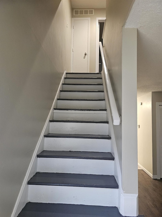 staircase with visible vents, baseboards, and wood finished floors