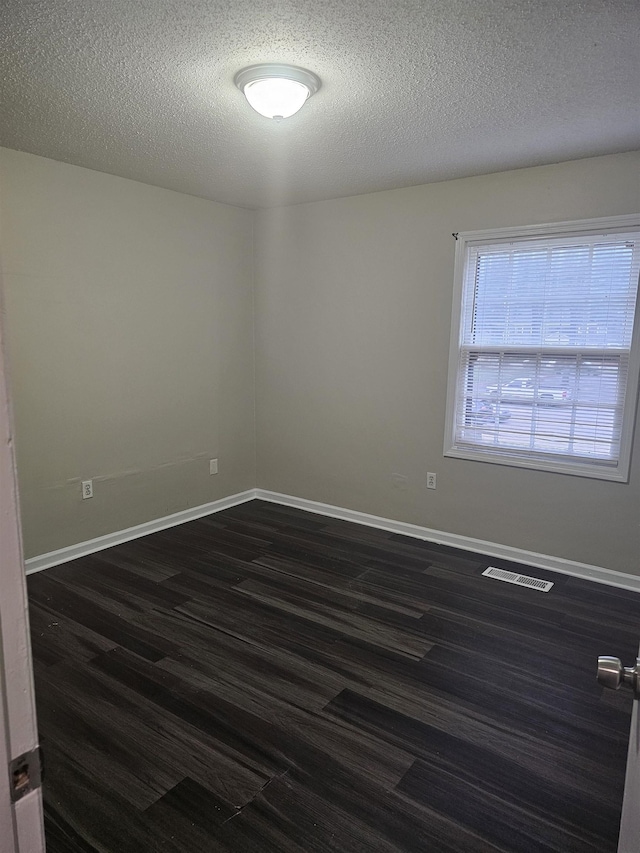 spare room featuring a textured ceiling, baseboards, visible vents, and dark wood-type flooring