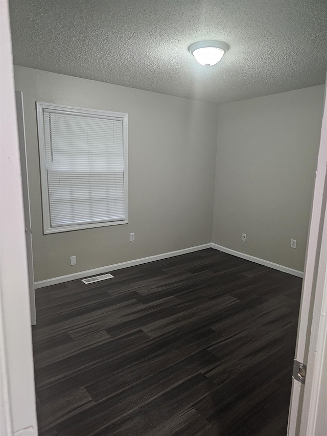 empty room featuring visible vents, a textured ceiling, baseboards, and dark wood-style floors