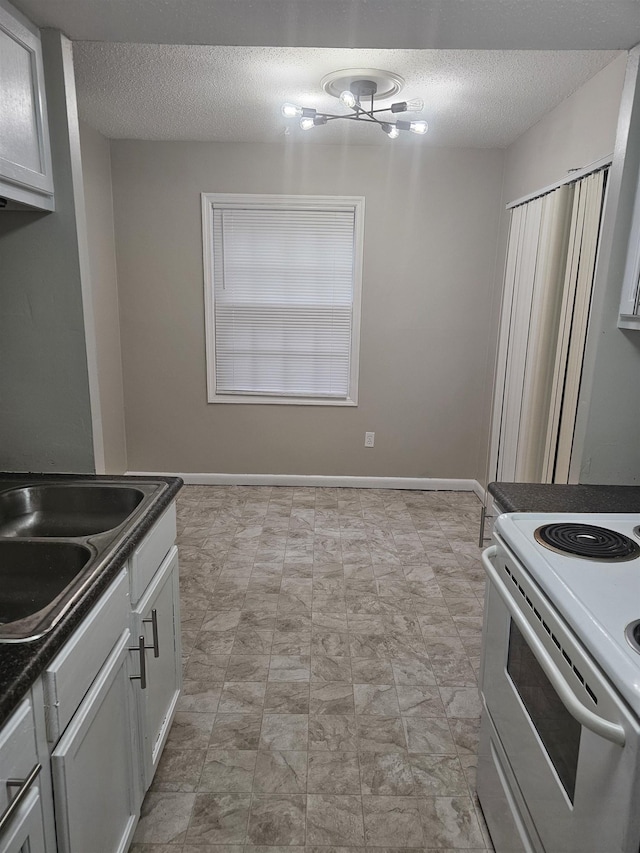 kitchen featuring electric range, a textured ceiling, dark countertops, a sink, and baseboards