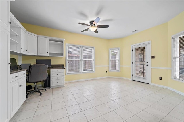 unfurnished office with plenty of natural light, a ceiling fan, built in desk, and visible vents