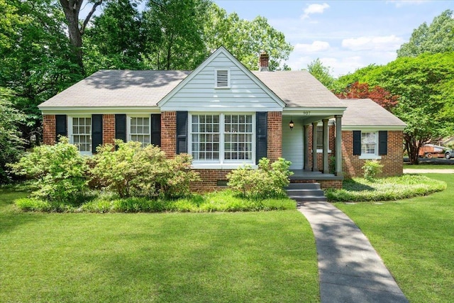 view of front of house with roof with shingles, a front lawn, brick siding, a chimney, and covered porch