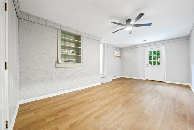 spare room featuring baseboards, ceiling fan, and brick wall