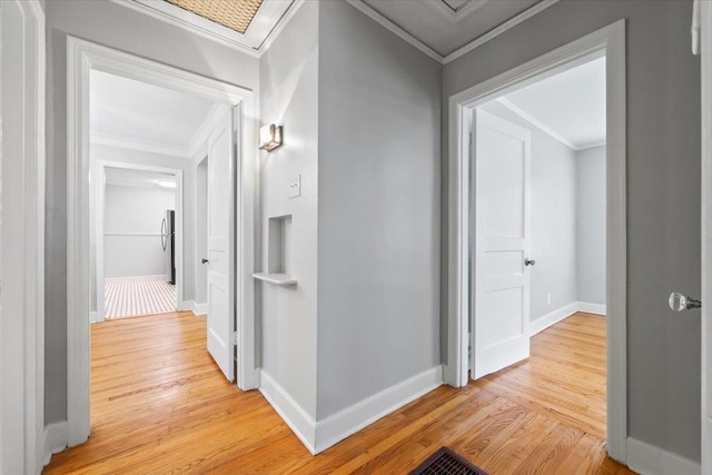 hall with light wood-type flooring, ornamental molding, and baseboards