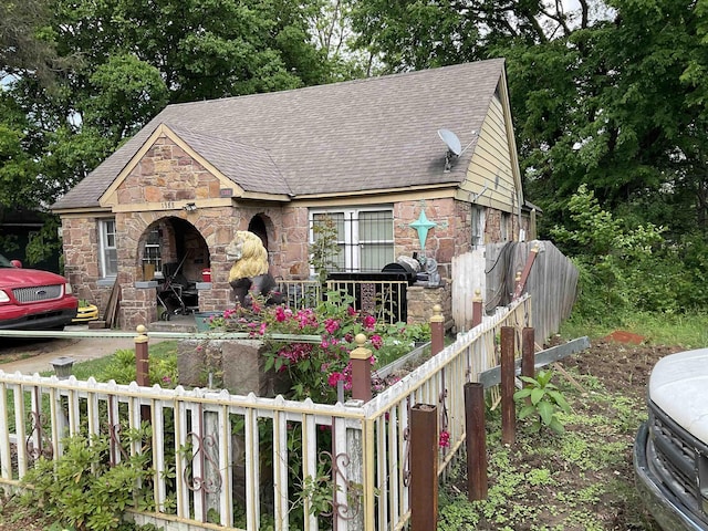 view of front of house with roof with shingles, fence, and stone siding
