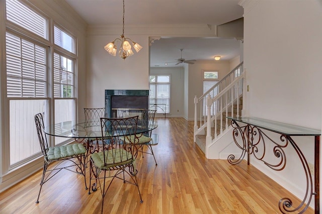 dining space featuring ornamental molding, stairs, light wood-style floors, ceiling fan, and a multi sided fireplace