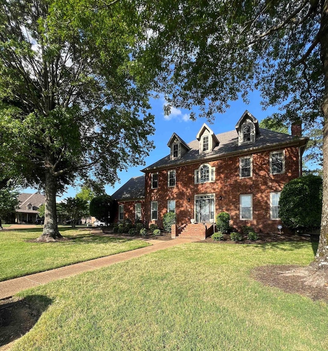 view of front facade featuring a chimney, a front lawn, and brick siding