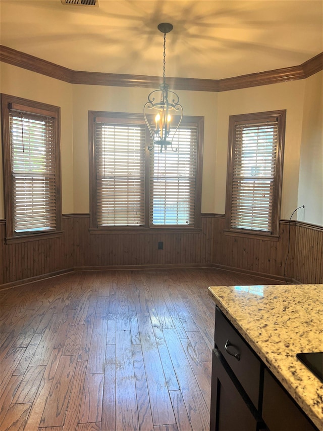 unfurnished dining area featuring a wainscoted wall, wood walls, hardwood / wood-style floors, and a notable chandelier