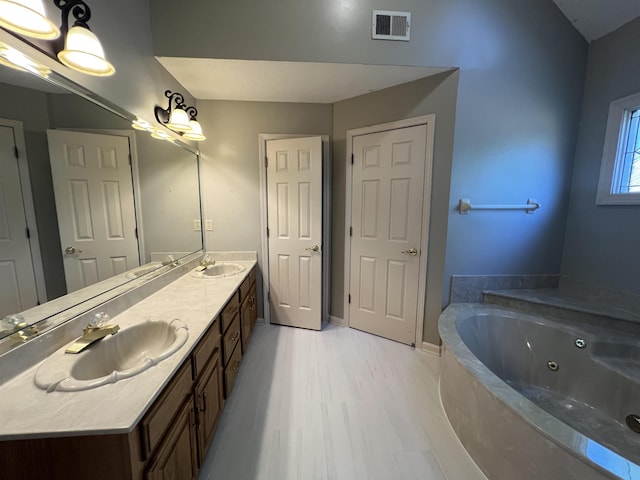 full bath featuring a sink, double vanity, a jetted tub, wood finished floors, and visible vents