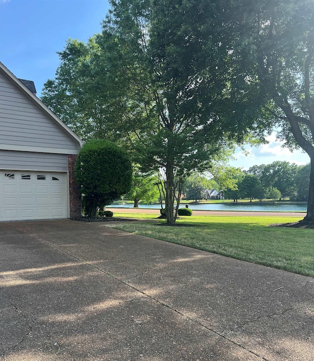exterior space featuring brick siding, a garage, a water view, concrete driveway, and a lawn