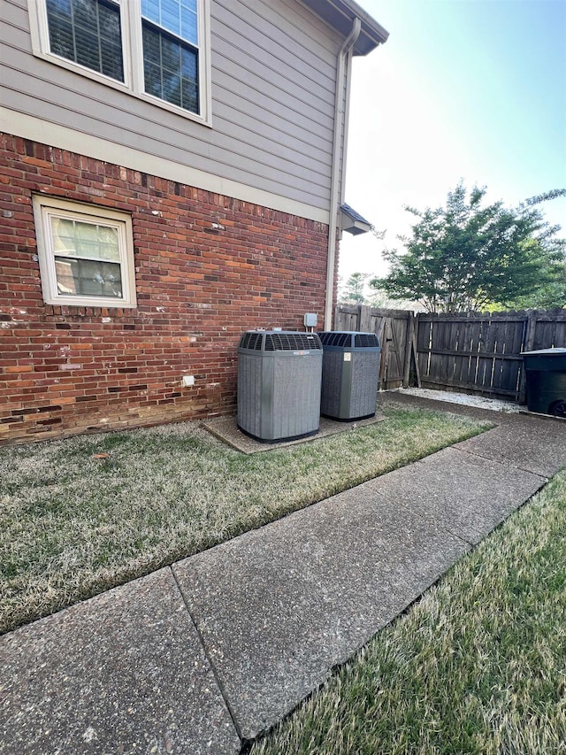 exterior space with brick siding, central AC unit, fence, and a yard