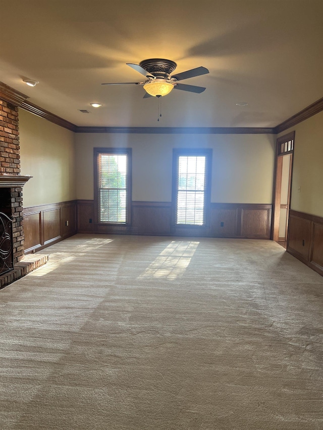 unfurnished living room featuring crown molding, carpet flooring, ceiling fan, and a wainscoted wall