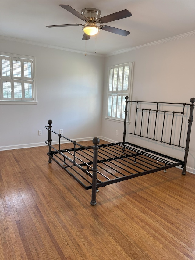 unfurnished bedroom featuring wood finished floors, multiple windows, ornamental molding, and baseboards