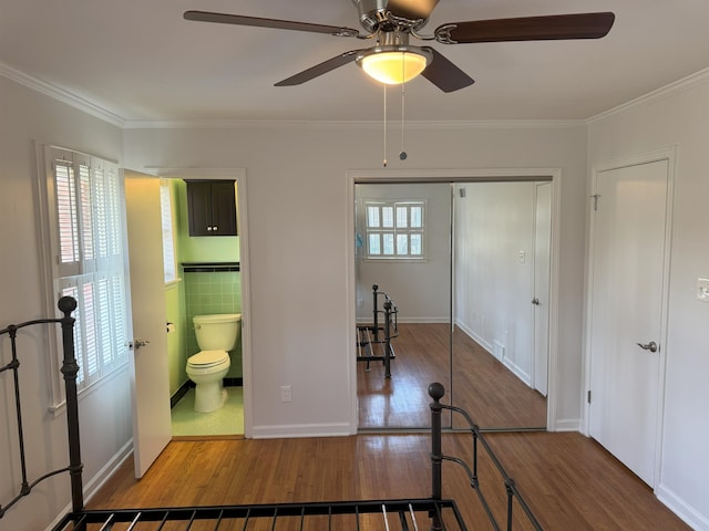 bedroom featuring wood finished floors, ornamental molding, a closet, ensuite bathroom, and ceiling fan