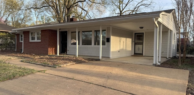 ranch-style home featuring concrete driveway, a chimney, a carport, and brick siding