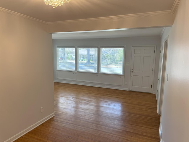 empty room with wood finished floors, ornamental molding, baseboards, and a chandelier