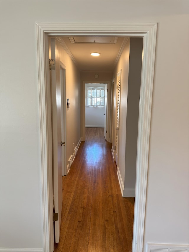 hallway featuring crown molding, wood finished floors, baseboards, and attic access