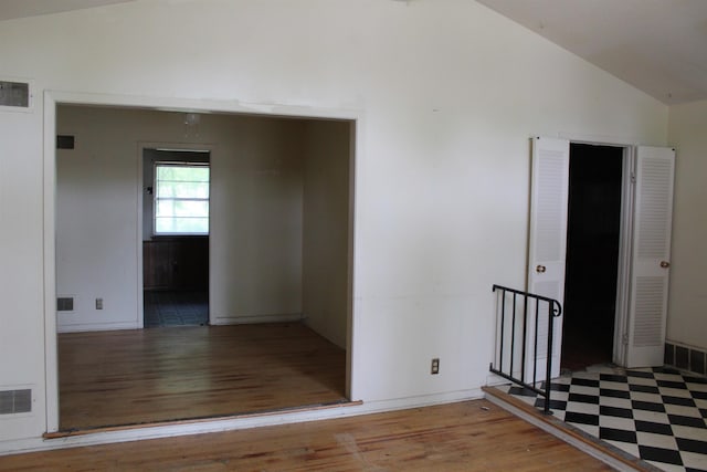 hall featuring baseboards, visible vents, wood finished floors, and lofted ceiling