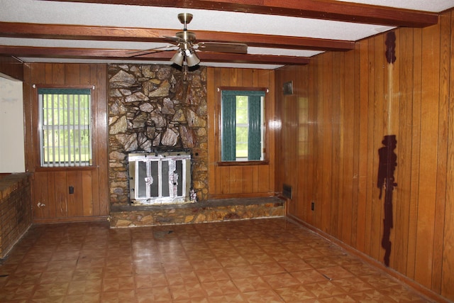 unfurnished living room with wooden walls, beam ceiling, ceiling fan, and a healthy amount of sunlight