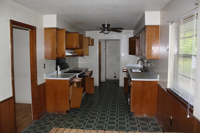 kitchen featuring brown cabinetry, a ceiling fan, dark floors, range with gas cooktop, and a sink