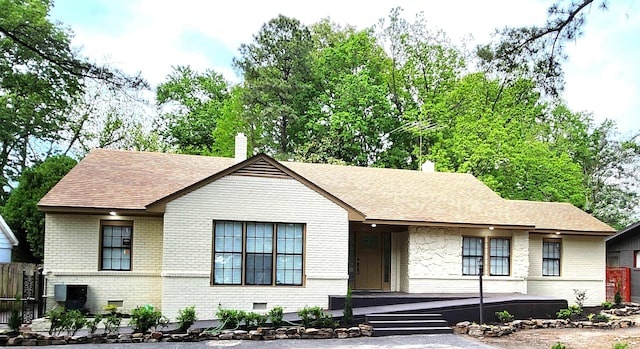 ranch-style house featuring roof with shingles, a chimney, and brick siding