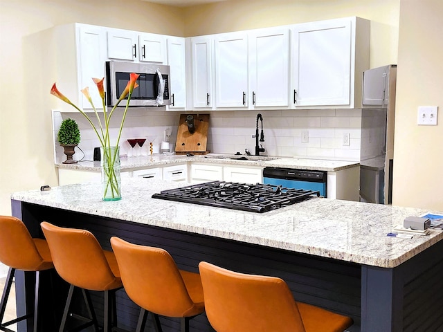 kitchen featuring a sink, white cabinetry, stainless steel microwave, backsplash, and dishwashing machine