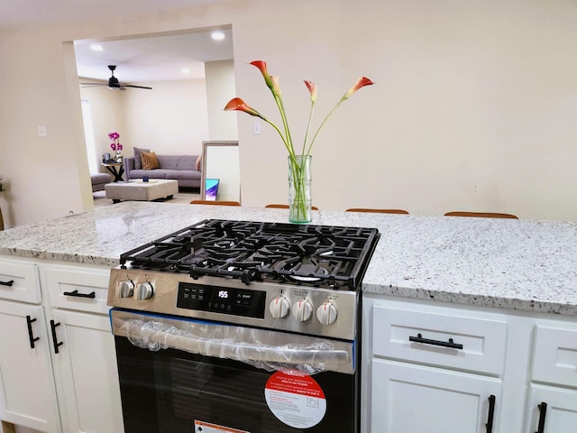 kitchen featuring stainless steel gas range, a ceiling fan, white cabinets, and light stone counters