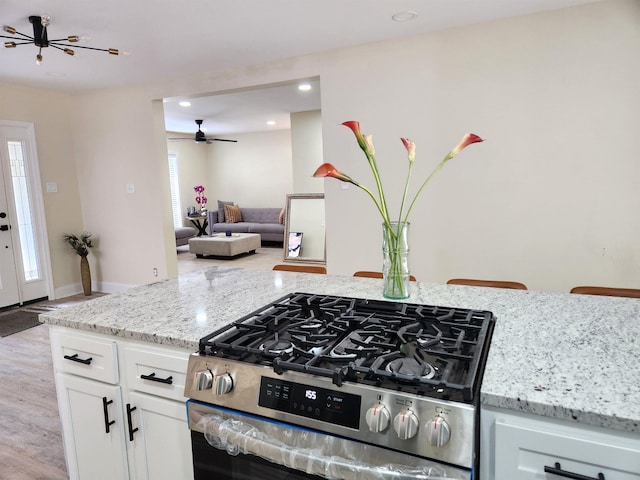 kitchen with stainless steel gas range, ceiling fan, light stone counters, light wood-style floors, and white cabinetry