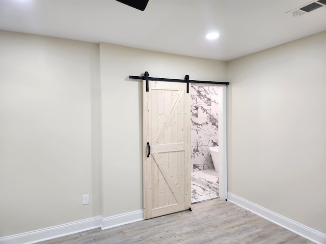 interior space with visible vents, wood finished floors, a barn door, baseboards, and recessed lighting