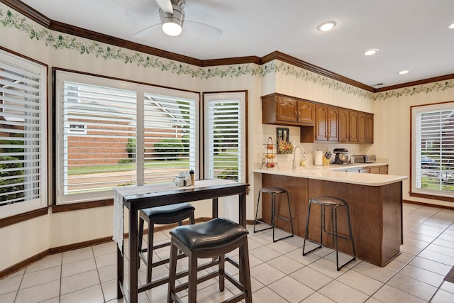 kitchen featuring a peninsula, crown molding, light countertops, a ceiling fan, and light tile patterned floors
