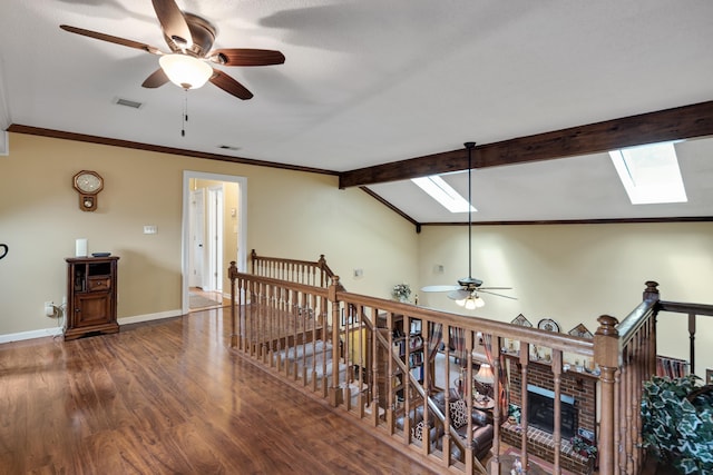 hallway with baseboards, visible vents, wood finished floors, an upstairs landing, and vaulted ceiling with skylight